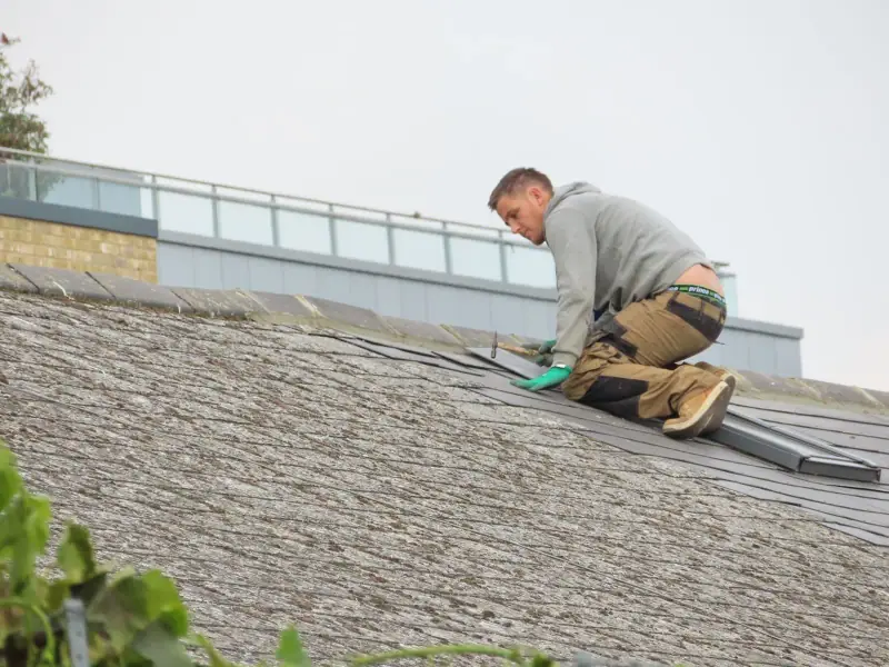 Roofer kneeling on a roof to replace damaged shingles