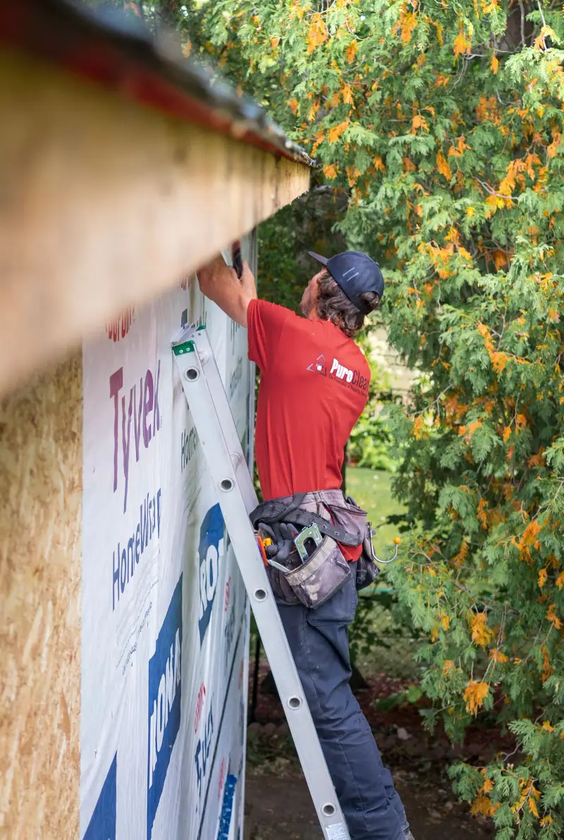 Installer on a ladder fitting housewrap before new siding